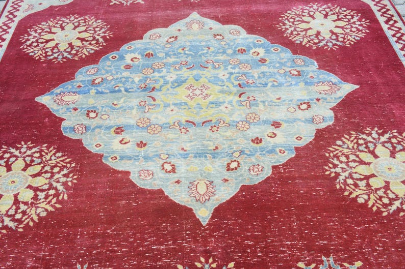 May include: A red rug with a blue and white floral pattern in the center. The rug has a distressed look and is made of wool.