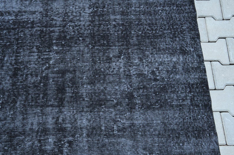 May include: A rectangular area rug featuring a deep black and charcoal gray color palette with a distressed, weathered texture. The surface displays a dense, woven grid pattern with visible signs of wear, creating a mottled appearance across the fabric.