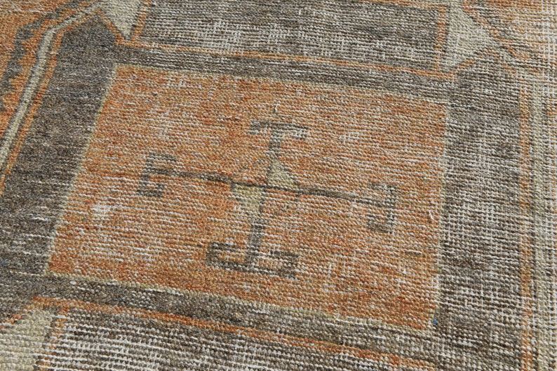 K&ouml;nnte beinhalten: Nahaufnahme eines braunen und grauen gewebten Teppichs mit geometrischem Muster. Der Teppich hat einen abgenutzten Look und eine verblasste orange Farbe in der Mitte.