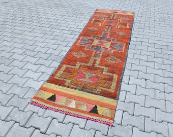 May include: A long, narrow, orange, red, and yellow patterned rug with a geometric design. The rug has a pink fringe.