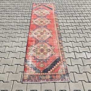 May include: A vintage red, blue, and cream runner rug with a floral pattern. The rug has a distressed look and is made of wool.