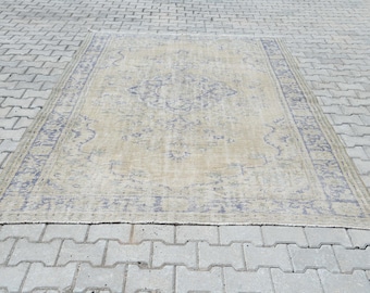 Op de afbeelding: Rechthoekig beige tapijt met een centraal medaillonontwerp en een blauwe rand. Het tapijt, geplaatst op een grijs bakstenen oppervlak, toont ingewikkelde patronen en een verouderde uitstraling. Het ontwerp bevat bloemmotieven.