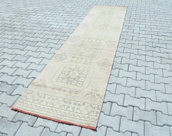 May include: A long, off-white runner rug with a geometric pattern. The rug has a subtle, faded look and features a repeating design of squares and diamonds.