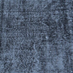May include: A woven textile rug featuring a distressed, mottled pattern in shades of deep black and faded charcoal gray. The surface displays a dense, uniform grid of small, interconnected fibers with visible areas of lighter, worn-out texture.