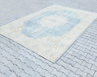 Könnte beinhalten: Ein hellblauer und cremefarbener Vintage-Teppich mit Blumenmuster. Der Teppich hat einen abgenutzten Look und liegt auf einer grauen Betonfläche.