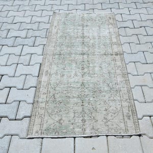 May include: A rectangular area rug featuring a faded sage green and light gray color palette. The rug displays a detailed, symmetrical floral and geometric pattern throughout its surface, framed by a distinct border with intricate linear motifs.