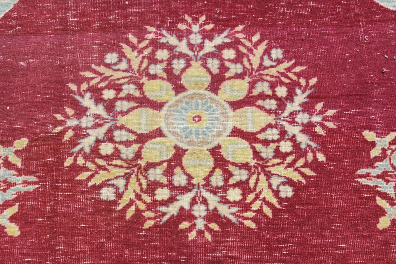May include: A red rug with a large, intricate floral design in shades of cream, beige, and blue. The design features a central medallion with a smaller circle in the center.