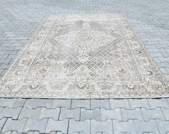 Op de afbeelding: Een rechthoekig tapijt in beige tinten, met een ingewikkeld, symmetrisch patroon. Het tapijt heeft een centraal ruitmotief en decoratieve randen. Het ligt op een grijs, in elkaar grijpend bestratingsoppervlak, dat het gedetailleerde ontwerp en de textuur benadrukt.