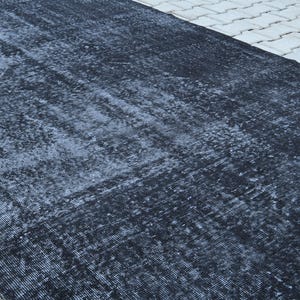 May include: A rectangular area rug featuring a deep black and charcoal gray color palette. The surface displays a distressed, weathered texture with subtle variations in tone and a faded, intricate pattern woven throughout the fabric material.