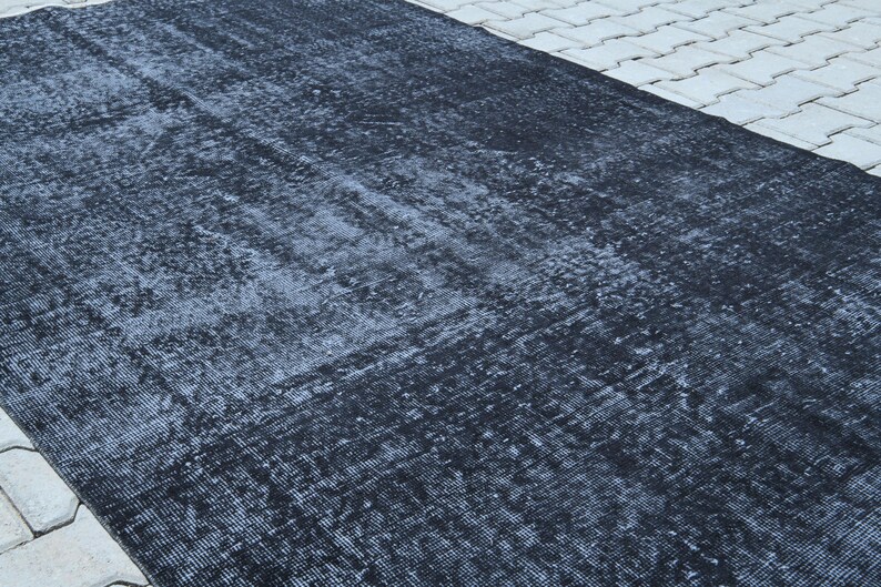 May include: A rectangular area rug featuring a deep black and charcoal gray color palette. The surface displays a distressed, weathered texture with subtle variations in tone and a faded, intricate pattern woven throughout the fabric material.