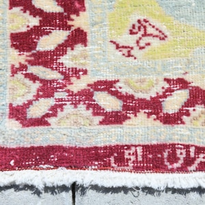 May include: Close-up of a rug with a white background and a red border. The rug has a floral pattern in shades of yellow, blue, and red.