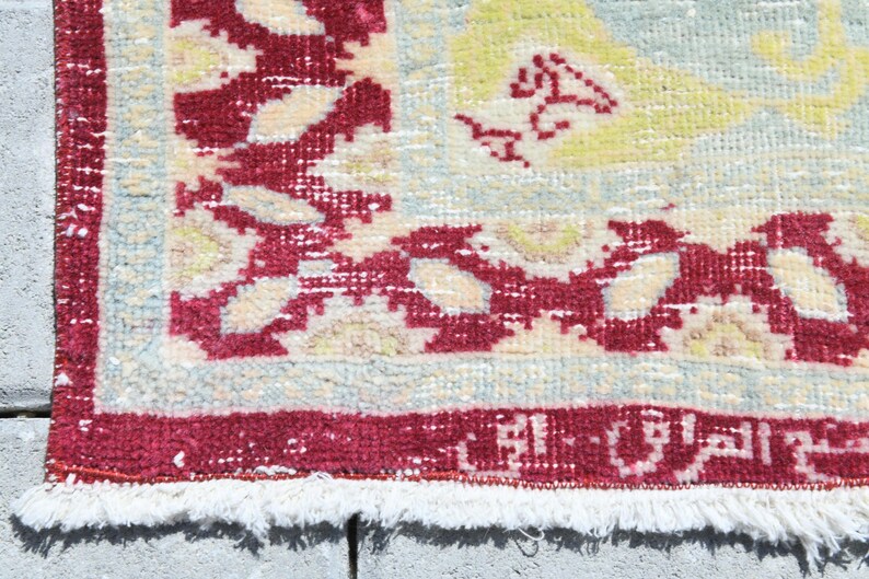 May include: Close-up of a rug with a white background and a red border. The rug has a floral pattern in shades of yellow, blue, and red.