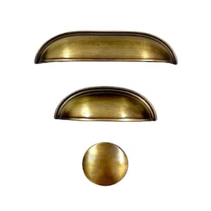 Puede incluir: Tres tiradores de armario de latón antiguo, dos son arqueados y uno es redondo.