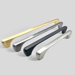 May include: Four cabinet pulls in different finishes: gold, silver, black, and nickel. The pulls are all the same shape, with a curved, modern design.