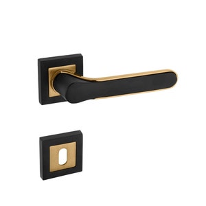 Op de afbeelding: Zwarte en gouden deurknop met een vierkante rozet en een sleutelgat. De knop is van metaal en heeft een modern ontwerp.