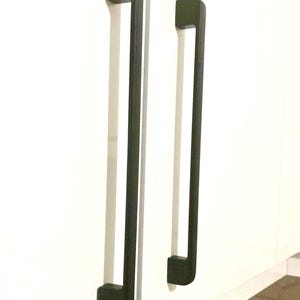 May include: Two matte black cabinet pulls with a long, vertical, rectangular design. Each handle features a flat front surface and two mounting points that attach to the white cabinet doors, creating a clean, uniform look for the cabinetry.