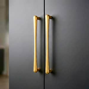 May include: Two vertical, elongated, cylindrical cabinet handles with a smooth, brushed gold finish. The handles are mounted onto a matte dark gray cabinet door surface, featuring a simple, slender design with rounded ends and a uniform thickness.