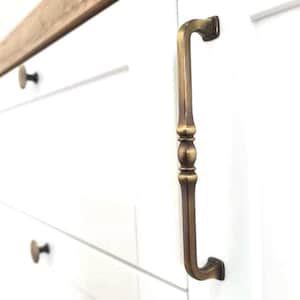 Peut inclure: Une poignée de porte de placard en laiton avec un design décoratif. La poignée est fixée à une porte de placard blanche.