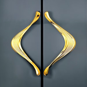 May include: A pair of gold-colored cabinet door handles with a unique, wave-like design.