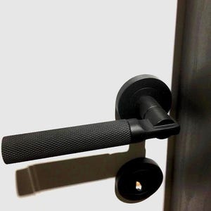 May include: Black door handle with a textured grip and a round, black knob. The handle is mounted on a white door.