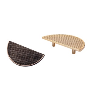 May include: Two half-circle cabinet pulls with a woven pattern. The pull on the left is black and the pull on the right is gold.