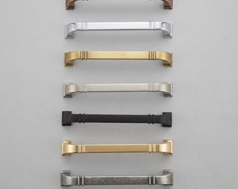 Peut inclure: Une collection de sept poignées de placard horizontales disposées en colonne verticale. Chaque poignée présente un design à barre droite avec deux nervures verticales près des extrémités et des bases de montage carrées. Les finitions incluent le cuivre, le chrome, le laiton, le nickel, le noir mat, l'or et l'argent antique.