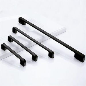 May include: Four black metal cabinet pulls of varying lengths. The pulls have a rectangular shape with rounded edges.