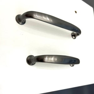 May include: Two black metal cabinet pulls with a brushed finish. The larger pull is approximately 10 cm long and the smaller pull is approximately 7.5 cm long.