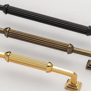 May include: Three cabinet door pulls in different finishes: black, antique brass, and gold. Each pull has a square base and a fluted, cylindrical handle.