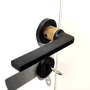 Peut inclure: Poignée de porte noire avec un bouton doré et un trou de serrure. La poignée est montée sur une porte en verre.