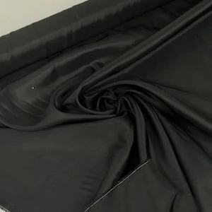 May include: Black satin fabric with a smooth, silky texture. The fabric is folded and draped, showcasing its luxurious feel.