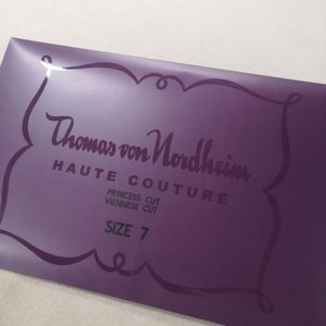 May include: A purple label featuring the text "Thomas von Nordheim HAUTE COUTURE" in a decorative font. The label also includes "PRINCESS CUT VIENNESE CUT" and "SIZE 7". The label has a decorative border.
