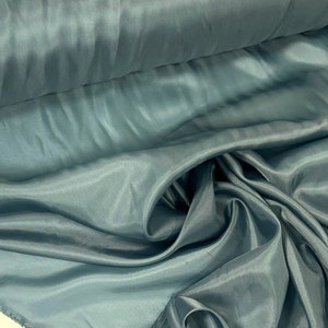 May include: A close-up of a light blue fabric with a smooth, silky texture. The fabric is folded and draped, showcasing its flowing nature.