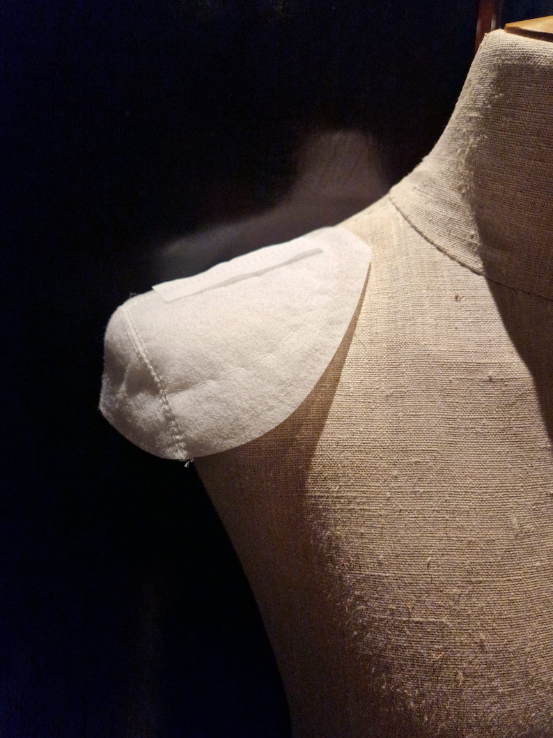 May include: A white fabric collar is pinned to a beige fabric dress form.