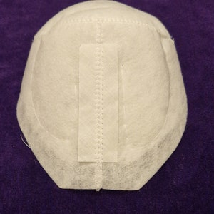 May include: White fabric dome with a seam down the center and a white fabric strip sewn on the front. The fabric is textured and has a slightly rough surface.