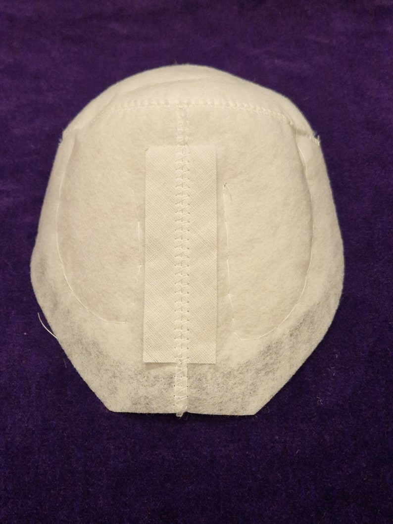 May include: White fabric dome with a seam down the center and a white fabric strip sewn on the front. The fabric is textured and has a slightly rough surface.