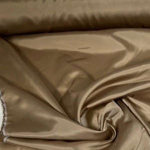 May include: A roll of smooth, silky, light brown fabric. The fabric has a subtle sheen and is perfect for sewing projects.