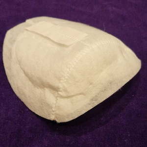 May include: White fabric filter with a sewn seam around the edge. The filter has a white label with a zig-zag stitch on the top.