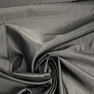 May include: A close-up of a smooth, dark gray fabric with a subtle sheen. The fabric is draped and folded, creating soft, flowing lines.
