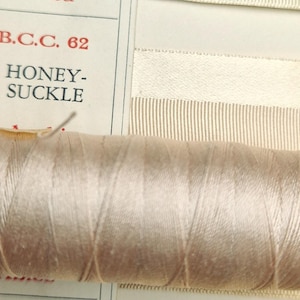 May include: A spool of beige thread with the text "B.C.C. 62 HONEY-SUCKLE" on a white label.