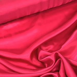 May include: A close-up of a bright red satin fabric. The fabric is smooth and silky, with a slight sheen. It is folded in a way that shows off its texture and drape.