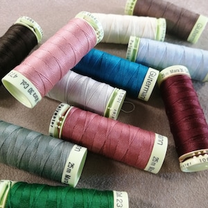 May include: A collection of spools of thread in various colours, including pink, green, blue, grey, and brown. The spools are labelled with the brand name "Gutermann" and the length of the thread in metres.