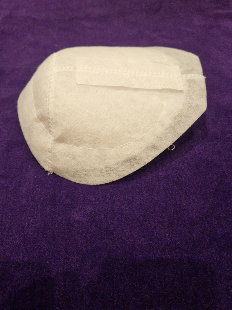 May include: White fabric cup with a stitched seam around the edge. The cup is on a purple surface.