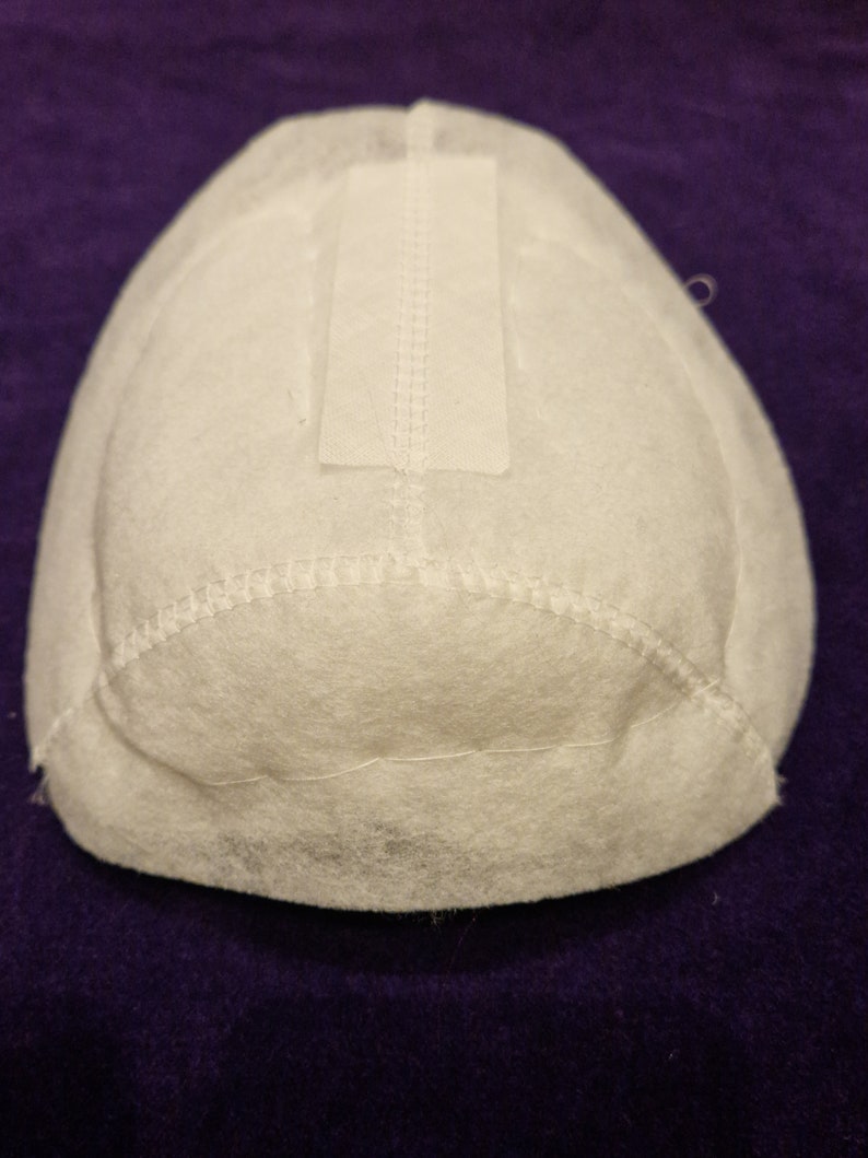 May include: White fabric filter with a white rectangular patch sewn on top. The filter is shaped like a dome and has a stitched edge.