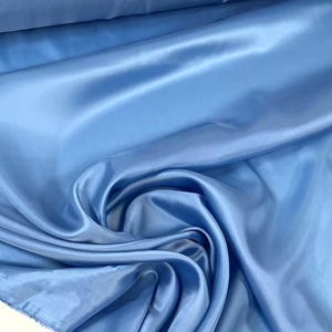 May include: A close-up shot of a light blue satin fabric. The fabric is draped and folded, creating soft shadows and highlights. The material has a smooth, shiny texture, reflecting light. The overall effect is one of luxury and elegance.