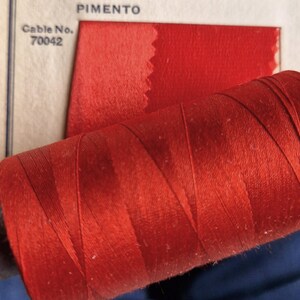 May include: A spool of red thread with the text "Cable No. 70042" and "PIMENTO" visible in the background.
