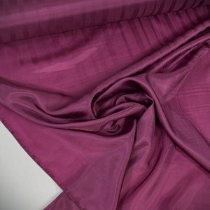 May include: A close-up of a deep purple fabric with a subtle striped pattern. The fabric is soft and flowing, with a luxurious feel.