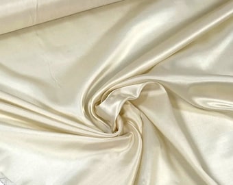 Puede incluir: Primer plano de una tela de satén lisa de color marfil. La tela está drapeada y doblada, mostrando su textura lujosa y su brillo sutil.