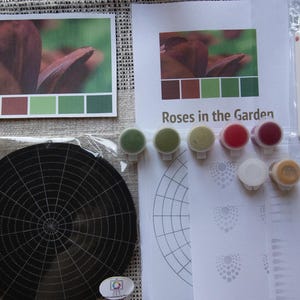 May include: Diamond painting kit featuring a close-up of a rose with the title "Roses in the Garden". The kit includes a black canvas with a grid, paint pots in shades of red, green, and brown, and tools for applying the diamonds.
