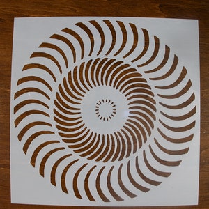 Può includere: Stencil in plastica bianca con un design circolare di cerchi concentrici. I cerchi sono formati da linee curve che creano un effetto vorticoso.